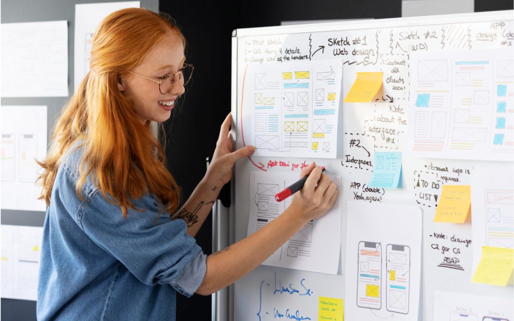 A woman is engaged in writing on a whiteboard, showcasing the essential planning and research for user-focused website development.