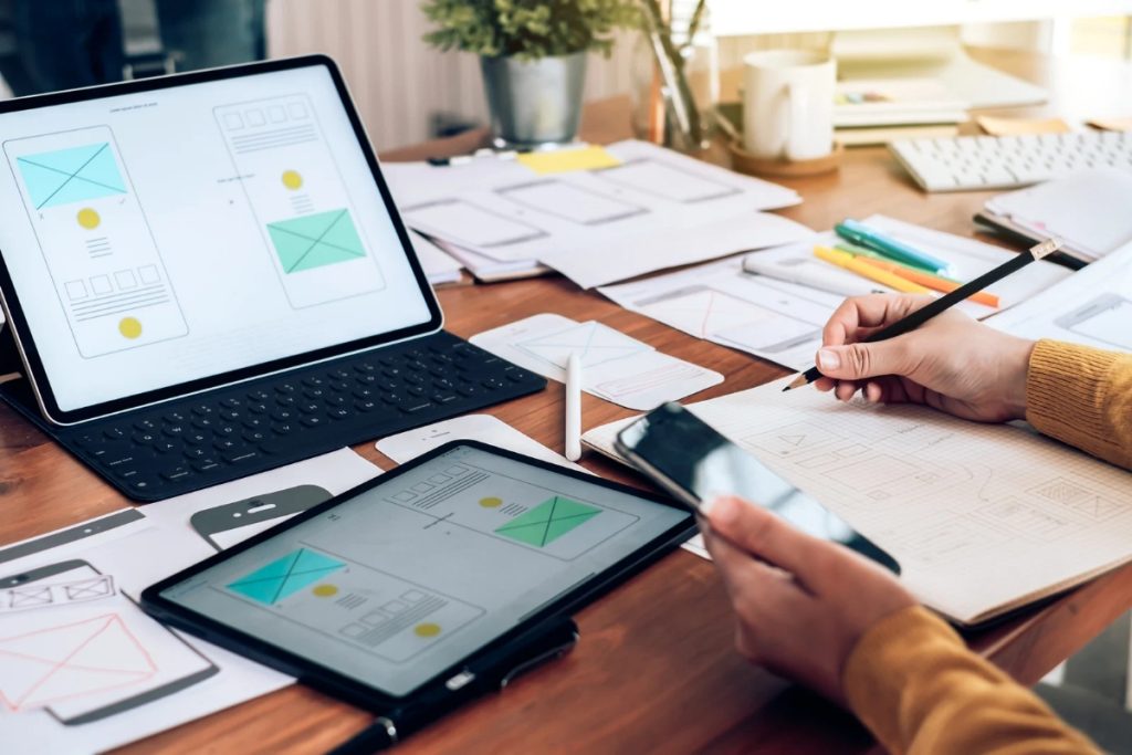 An individual works on a laptop and tablet at a desk, emphasizing the balance between UI and UX in their projects.